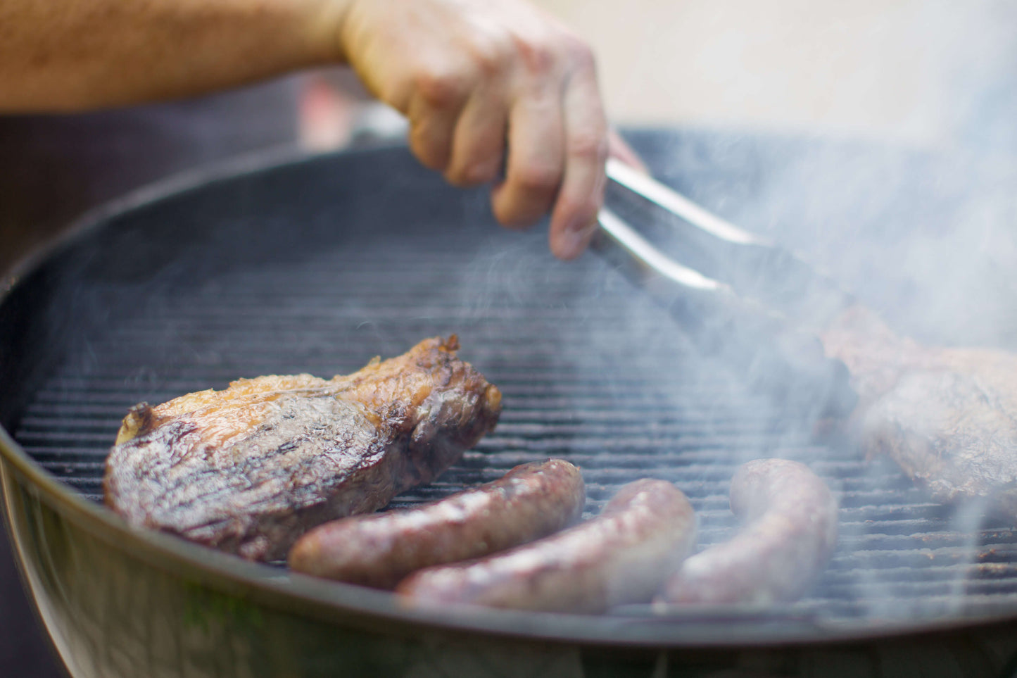 Sausages and meet on a grill with smoke rising. 