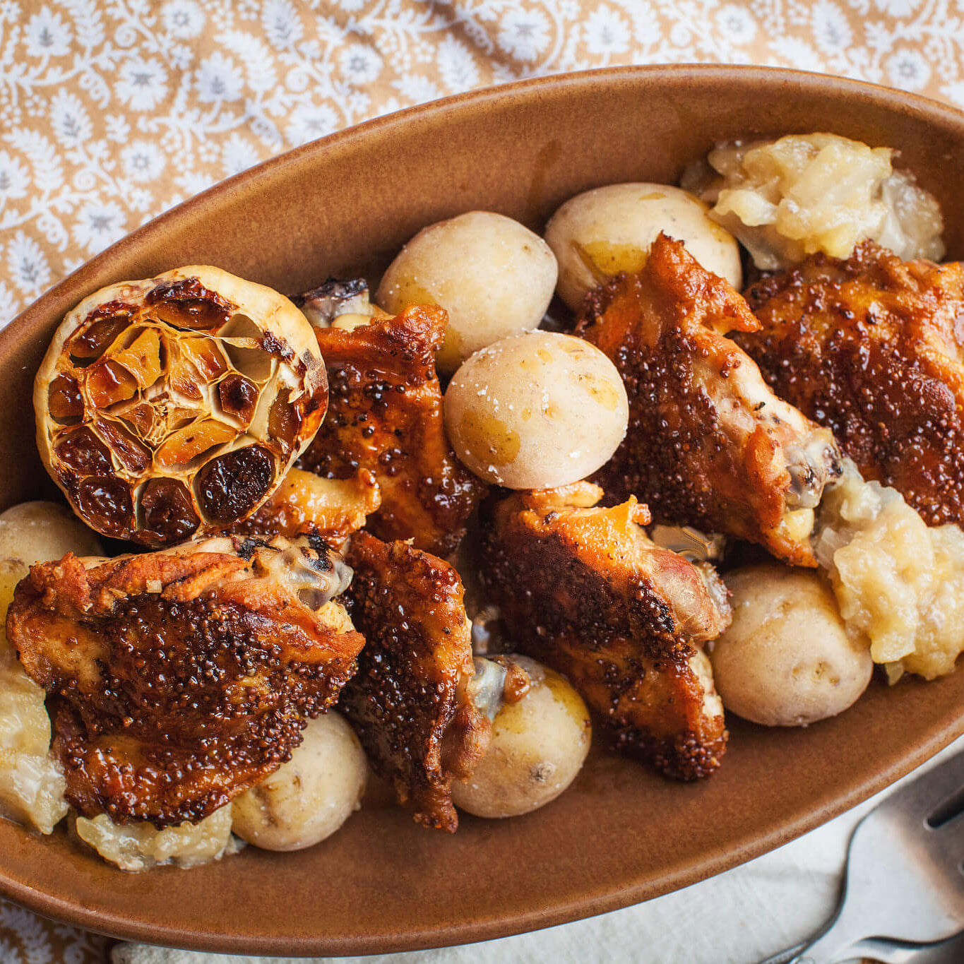 Dish of roasted chicken with potatoes and garlic on a patterned tablecloth