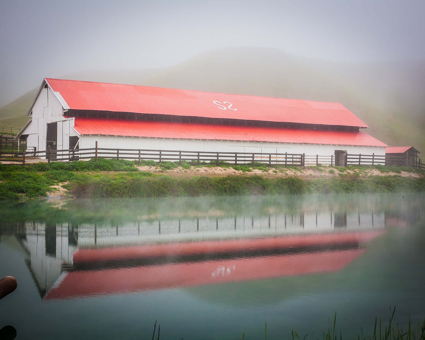 Red and white barn reflected in a misty pond with mountains in the background